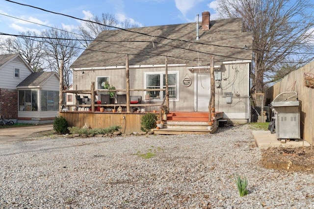 view of front of house featuring a shingled roof, a chimney, fence, and a deck