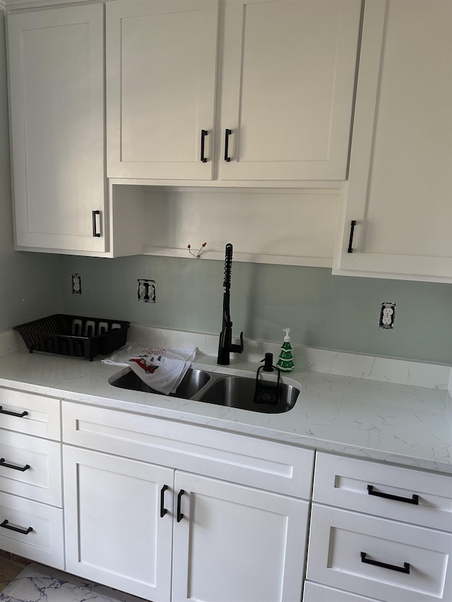 kitchen with white cabinetry, a sink, and light stone countertops