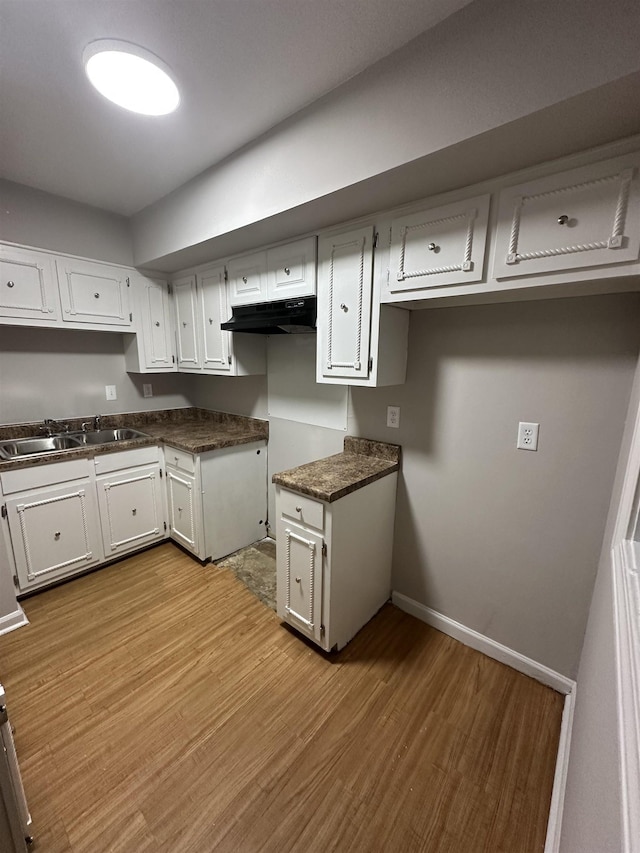 kitchen featuring dark countertops, white cabinets, a sink, light wood-type flooring, and baseboards