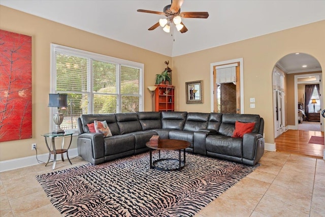 living area with light tile patterned floors, baseboards, arched walkways, and a ceiling fan