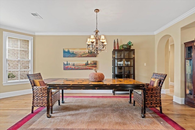 dining space featuring arched walkways, ornamental molding, wood finished floors, and a notable chandelier