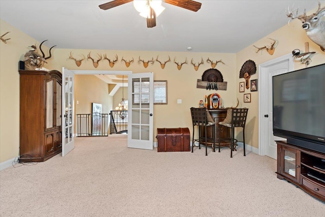 living area with french doors, a dry bar, light carpet, baseboards, and ceiling fan with notable chandelier