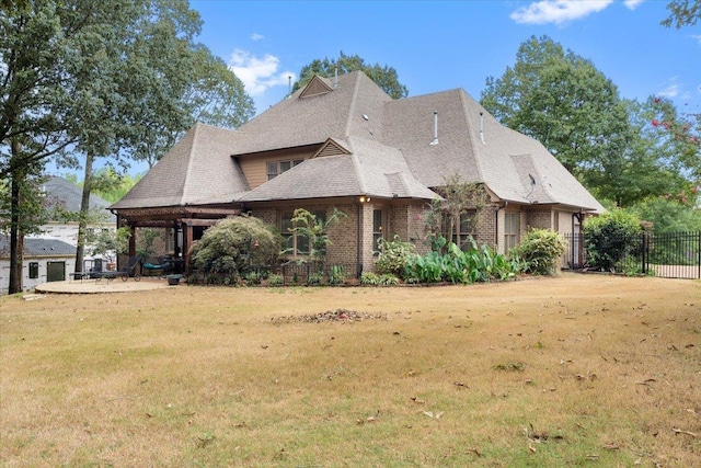 view of front of property featuring brick siding, roof with shingles, fence, and a front yard