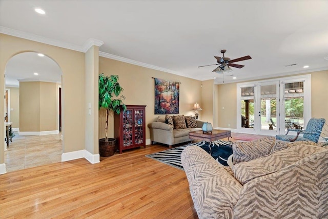 living area featuring baseboards, arched walkways, crown molding, light wood-style floors, and recessed lighting