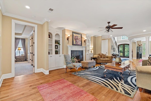 living area with ornamental molding, light wood-style flooring, a high end fireplace, and ornate columns