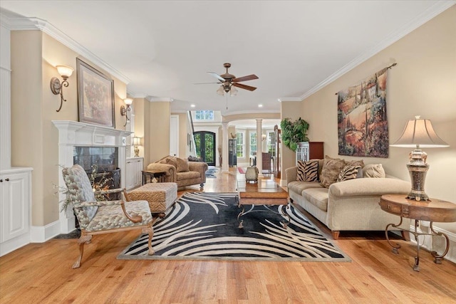 living room featuring arched walkways, a fireplace, light wood-style floors, ornamental molding, and decorative columns