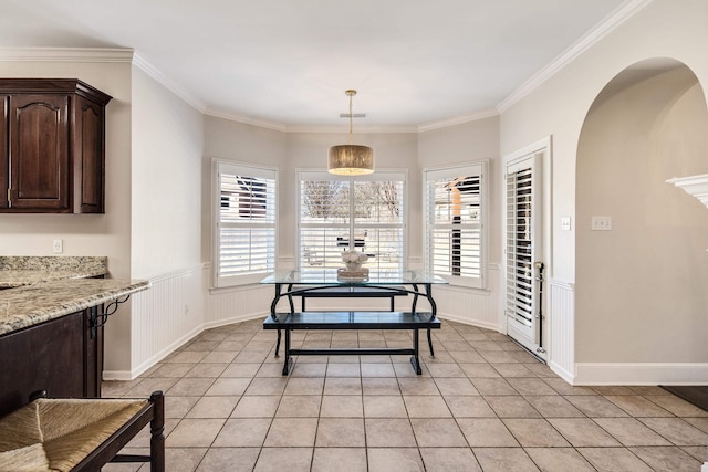 dining room featuring light tile patterned floors, plenty of natural light, ornamental molding, and wainscoting