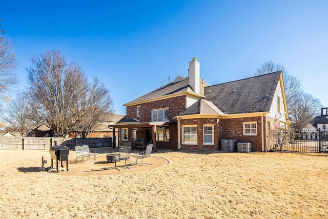 rear view of property with an outdoor fire pit, a fenced backyard, central air condition unit, a patio area, and brick siding