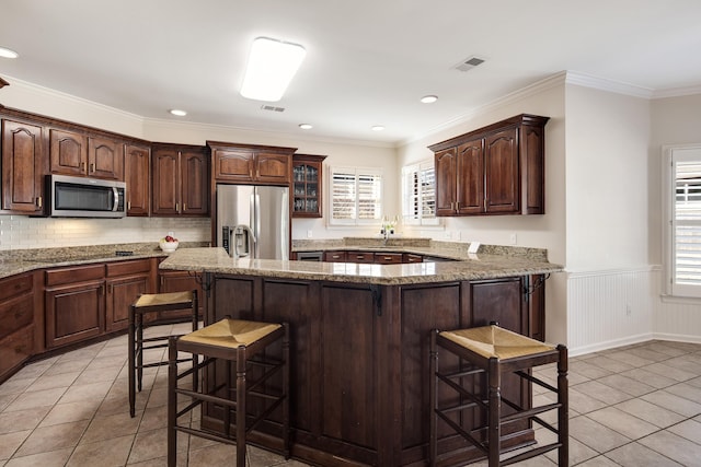 kitchen with dark brown cabinetry, visible vents, appliances with stainless steel finishes, and a breakfast bar