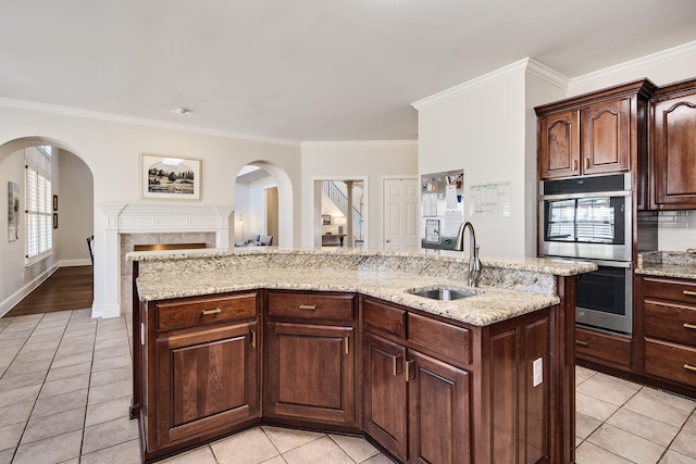 kitchen featuring ornamental molding, stainless steel double oven, open floor plan, a kitchen island with sink, and a sink