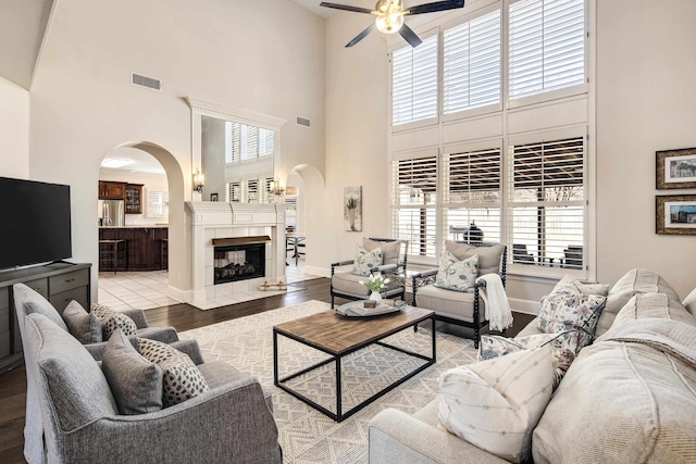 living room featuring arched walkways, visible vents, baseboards, light wood-type flooring, and a tiled fireplace