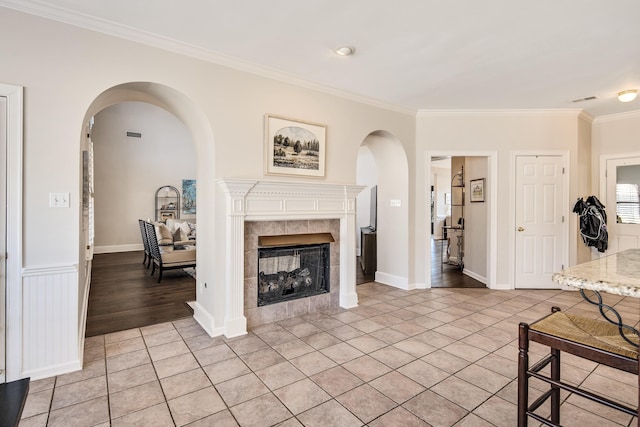 living room with arched walkways, crown molding, a fireplace, light tile patterned floors, and visible vents