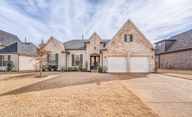 french country inspired facade featuring a garage, concrete driveway, brick siding, and a shingled roof