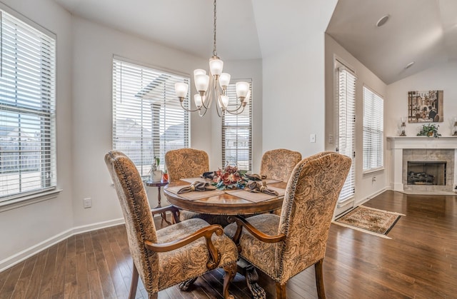 dining space with dark wood-style floors, vaulted ceiling, a tiled fireplace, and plenty of natural light