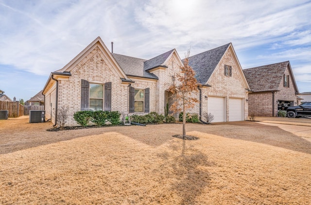 french country inspired facade with brick siding, a shingled roof, concrete driveway, central AC unit, and fence