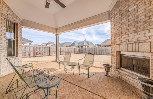 view of patio featuring an outdoor brick fireplace, a residential view, a fenced backyard, and a ceiling fan