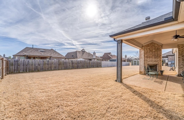 view of yard with an outdoor brick fireplace, a ceiling fan, a fenced backyard, a residential view, and a patio area