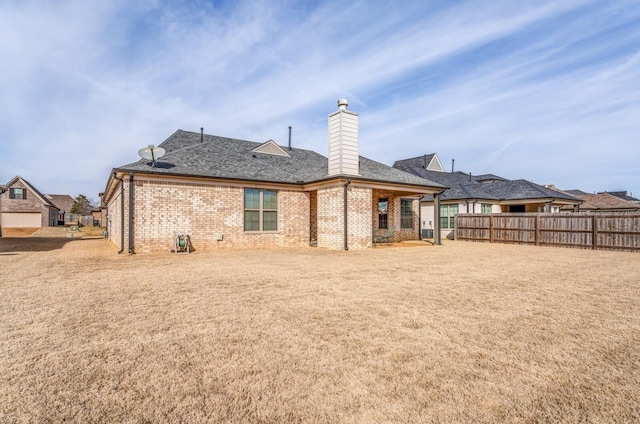 rear view of property featuring a shingled roof, brick siding, fence, and a chimney