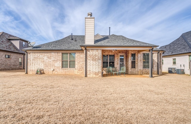 rear view of house featuring central air condition unit, brick siding, a patio, and roof with shingles