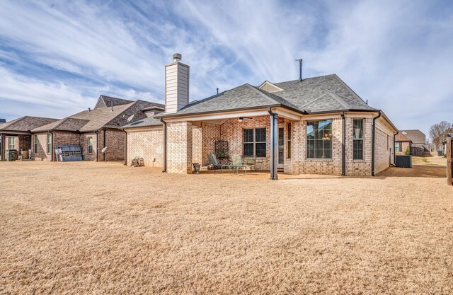 back of house with a jacuzzi, central AC, brick siding, a shingled roof, and a chimney