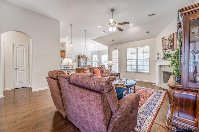 living room featuring dark wood finished floors, arched walkways, vaulted ceiling, and a tiled fireplace