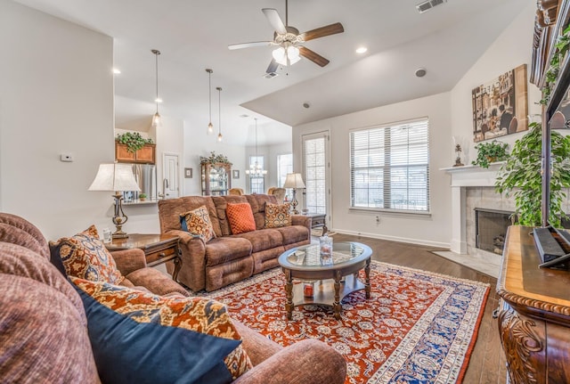 living area featuring lofted ceiling, ceiling fan with notable chandelier, a tiled fireplace, and wood finished floors