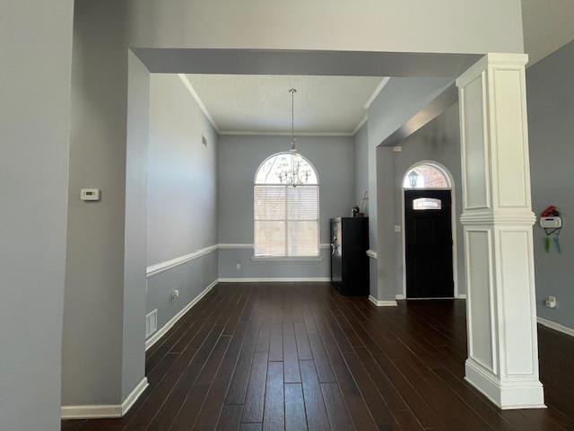 entrance foyer featuring baseboards, ornamental molding, dark wood-style flooring, ornate columns, and a chandelier