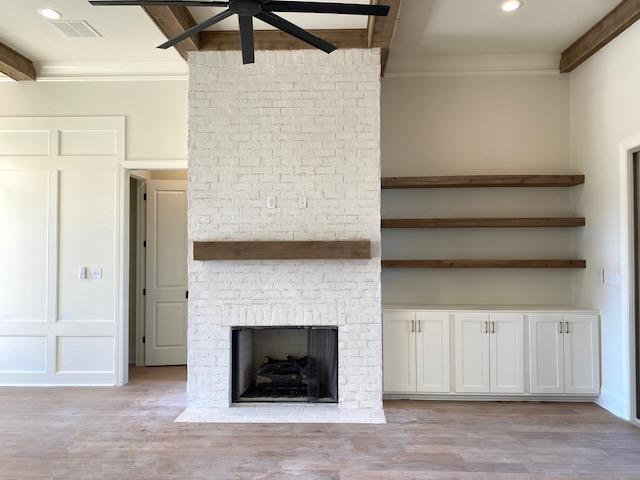 unfurnished living room with ceiling fan, a fireplace, visible vents, ornamental molding, and light wood finished floors