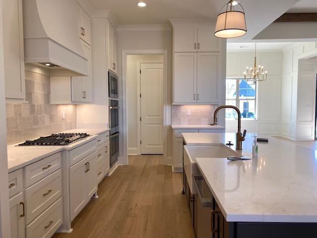 kitchen featuring white cabinets, appliances with stainless steel finishes, a kitchen island with sink, light wood-style floors, and premium range hood