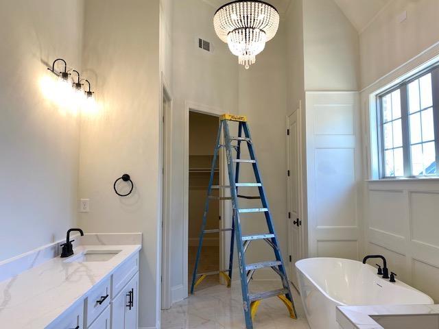 full bath with marble finish floor, visible vents, a decorative wall, a chandelier, and a freestanding tub