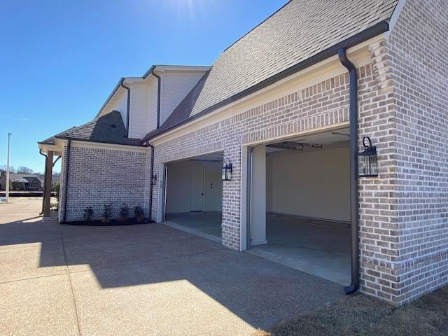 view of property exterior featuring brick siding, driveway, an attached garage, and roof with shingles