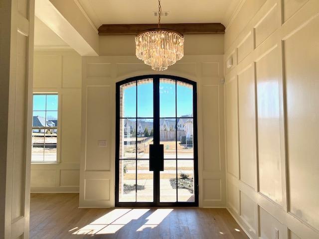 doorway to outside with crown molding, a chandelier, a decorative wall, and light wood-style flooring