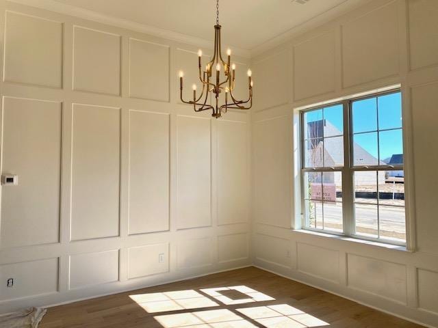 unfurnished dining area featuring an inviting chandelier, ornamental molding, a decorative wall, and wood finished floors