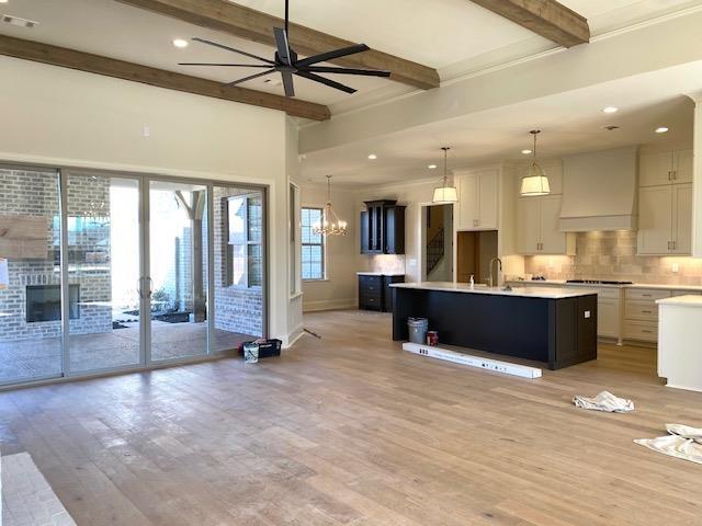 kitchen featuring open floor plan, beamed ceiling, custom exhaust hood, light countertops, and light wood-style floors