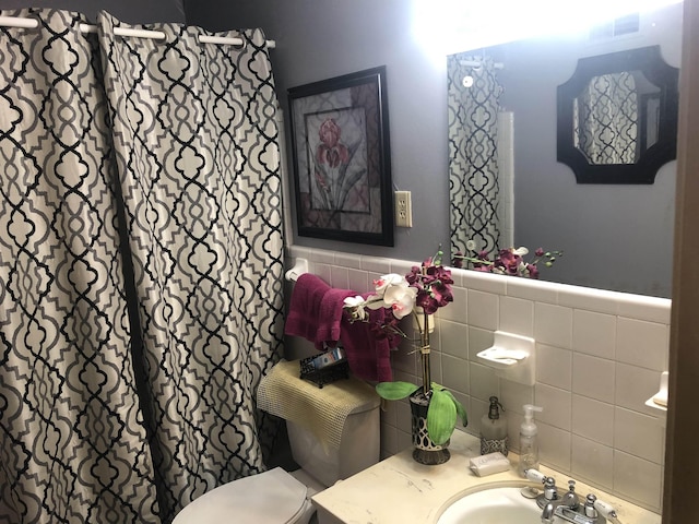 bathroom featuring wainscoting, tile walls, toilet, and vanity