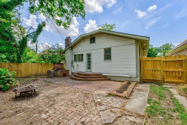 back of property featuring a fire pit, a fenced backyard, a chimney, a gate, and a patio area