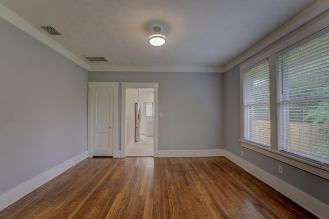 empty room featuring baseboards, visible vents, wood finished floors, and ornamental molding