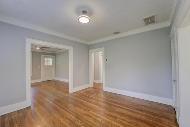 empty room featuring baseboards, wood finished floors, visible vents, and crown molding