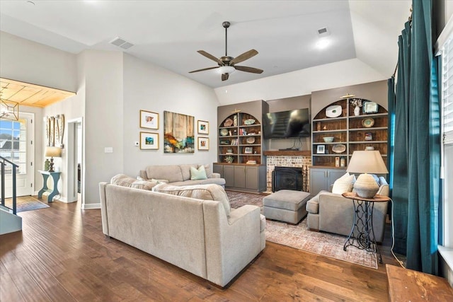 living area featuring built in features, lofted ceiling, visible vents, a brick fireplace, and wood finished floors