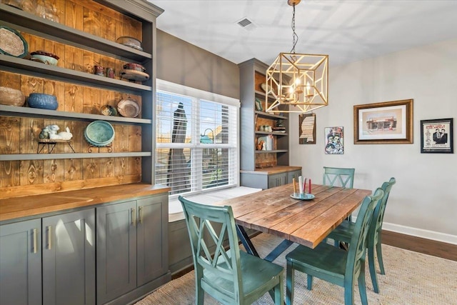 dining space with built in features, visible vents, baseboards, wood finished floors, and a notable chandelier