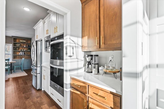 kitchen featuring stainless steel appliances, light countertops, brown cabinetry, dark wood-type flooring, and white cabinetry