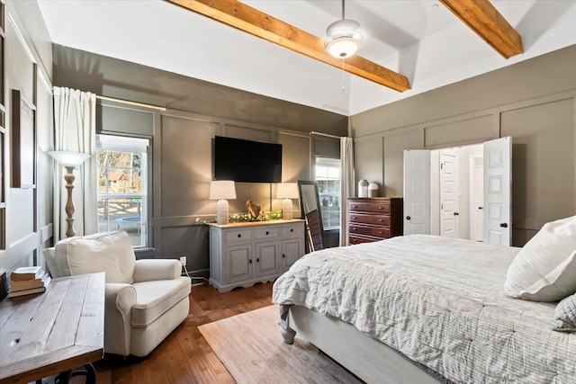 bedroom with ceiling fan, a decorative wall, beamed ceiling, and wood finished floors