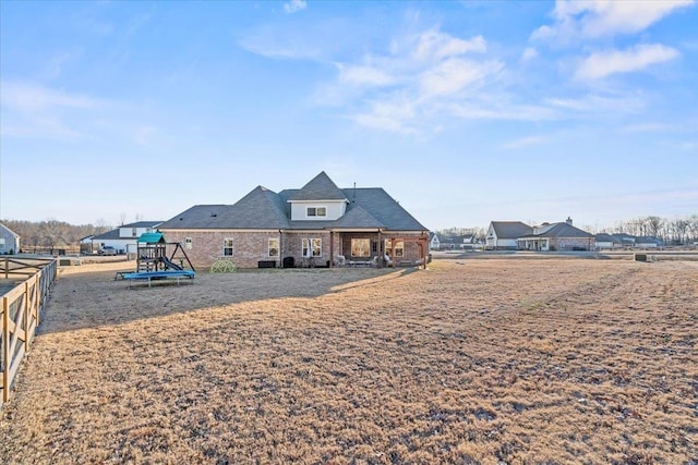 rear view of property featuring playground community and fence