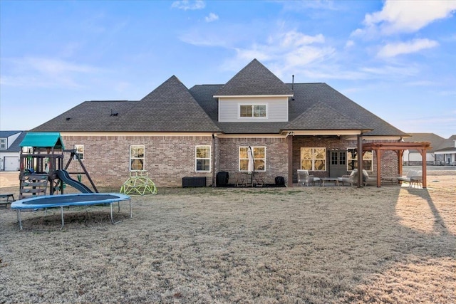 rear view of property with a trampoline, a playground, brick siding, a shingled roof, and central AC