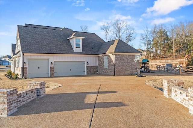 view of front of home with driveway, roof with shingles, a playground, board and batten siding, and brick siding