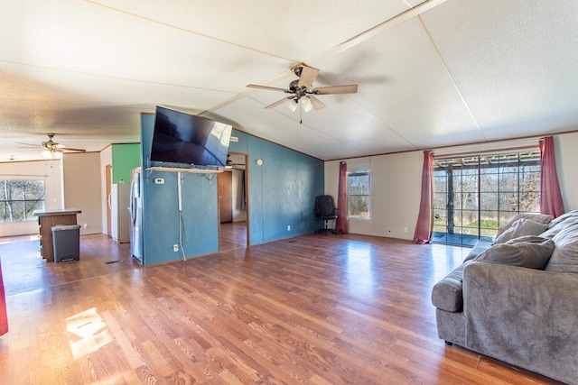 living area with ceiling fan, vaulted ceiling, a textured ceiling, and wood finished floors