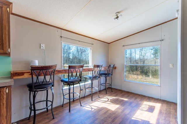 dining space with lofted ceiling, ornamental molding, a textured ceiling, and wood finished floors