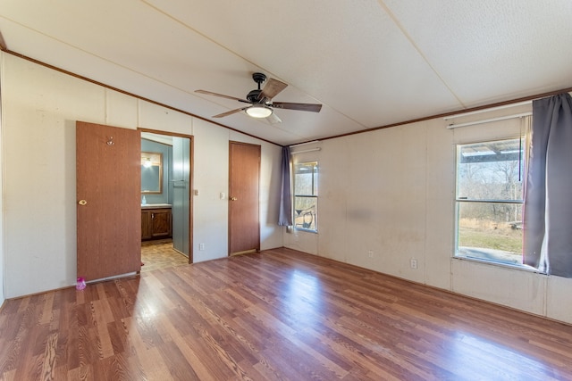 unfurnished bedroom with connected bathroom, multiple windows, vaulted ceiling, and wood finished floors