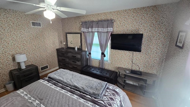 bedroom featuring a ceiling fan, wood finished floors, visible vents, and wallpapered walls