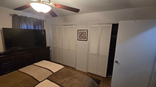 bedroom featuring a textured ceiling, ceiling fan, wood finished floors, and two closets